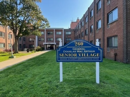 General Douglas Mac Arthur Senior Village sign at the entrance of a brick building.